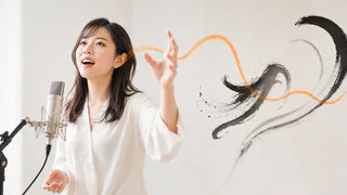 女性ボーカルがハンドイメージでメロディを手で描き、書道の筆運びをイメージして歌の表現力を高める様子
